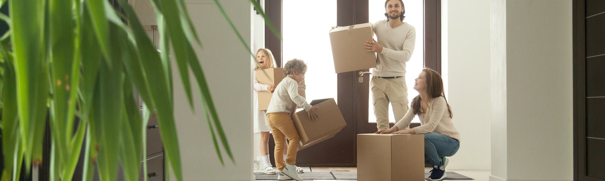 Mutter, Vater und zwei Kinder, die mit Kartons in das neue Haus einziehen.